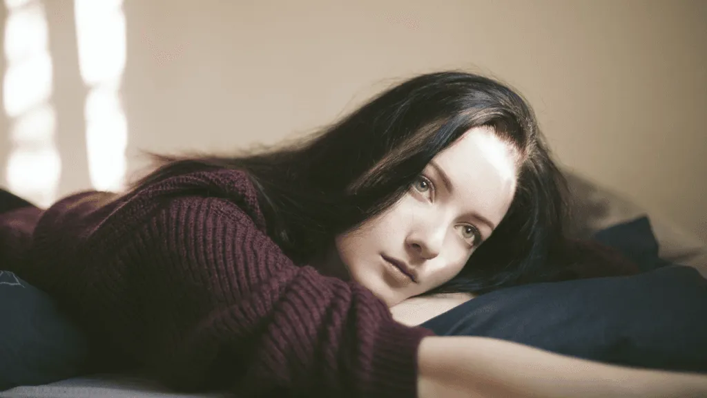A soulful young woman, her face etched with grief, gazes into the distance, her eyes brimming with tears. Around her, a hazy, dreamlike landscape unfolds, casting a melancholic atmosphere. Soft, muted colors and a shallow depth of field create a sense of emotional intensity, highlighting the woman's inner turmoil. The scene is lit by a warm, diffused light, casting gentle shadows and adding depth to the composition. The overall mood is one of profound sadness and the profound impact of a mother's passing, captured in a powerful, contemplative moment. Dreaming of Mom Dying Emotional Impact of These Dreams