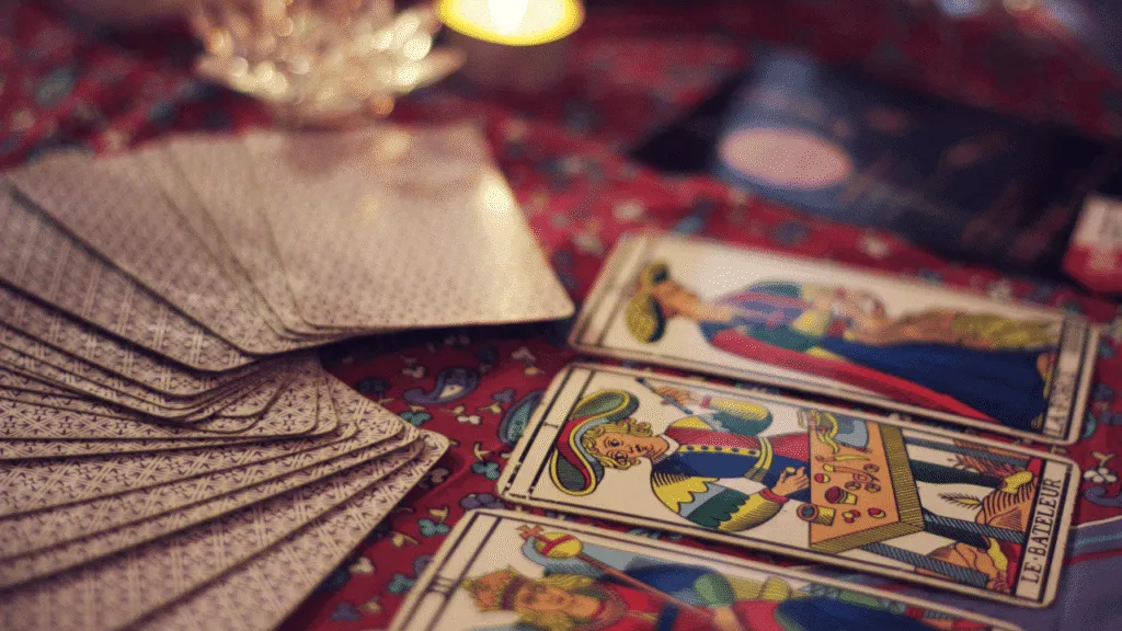 A dimly lit table, adorned with a velvet cloth, serves as the stage for an array of tarot cards. The cards, bearing intricate illustrations, are scattered artfully, inviting the viewer to delve into their mystical symbolism. Soft, warm lighting casts a gentle glow, creating an atmosphere of contemplation and introspection. In the foreground, a single tarot card stands out, its imagery capturing the essence of divination and the interpretation of one's fortune. The background is hazy, emphasizing the subject matter and drawing the viewer's focus to the cards themselves. The scene exudes a sense of ancient wisdom and the timeless allure of the tarot, perfectly capturing the essence of "How to Interpret Fortune Telling Cards". How to Interpret Name of Fortune Telling Cards
